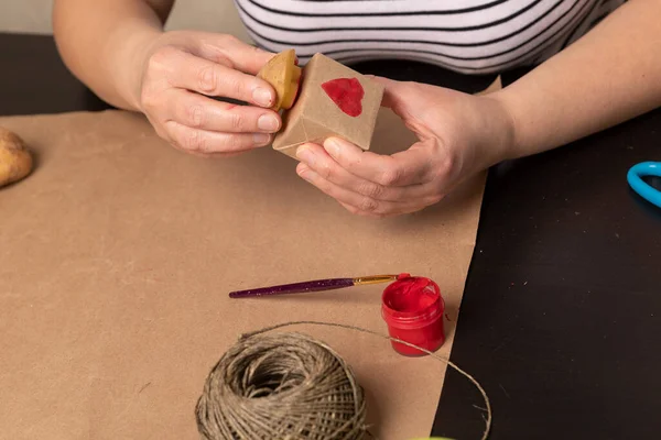Herzförmige Kartoffelmarke auf Bastelpapier. Der Prozess der Dekoration eines Geschenks zum Valentinstag. Vorbereitungen für das Fest am 14. Februar. — Stockfoto
