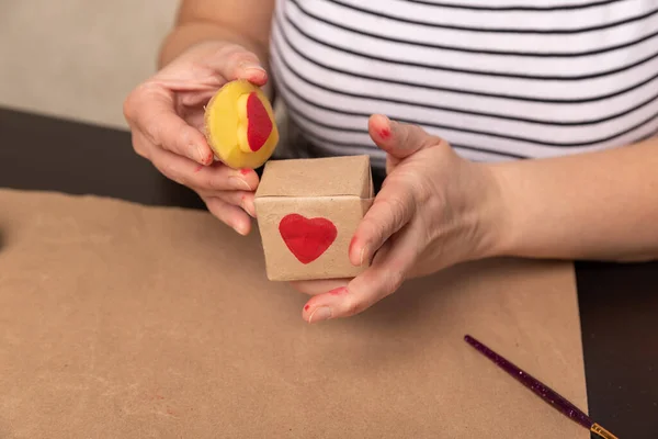 Sello de patata en forma de corazón en papel artesanal. El proceso de decorar un regalo para el Día de San Valentín. Preparándose para la celebración del 14 de febrero. — Foto de Stock