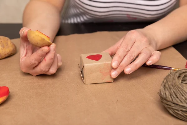 Σφραγίδα πατάτας σε σχήμα καρδιάς σε χαρτί χειροτεχνίας. Η διαδικασία της διακόσμησης ενός δώρου για την Ημέρα του Αγίου Βαλεντίνου. Ετοιμάζεται για τον εορτασμό στις 14 Φεβρουαρίου. — Φωτογραφία Αρχείου