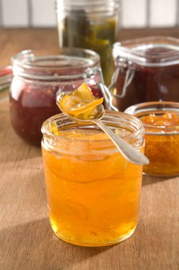 Reçel kavanozunun üstünde bir kaşık marmelat, arka planda çilek ve diğer reçeller..