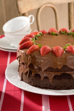 Çilekli çikolatalı kek çayla servis edilmeye hazır, arka planda bir sandalyeyle kırmızı keten masa örtüsü üzerinde..