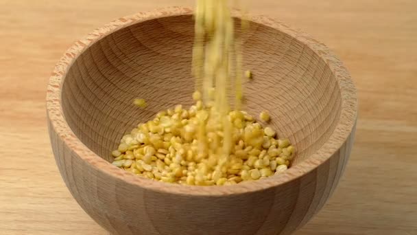 木製のテーブルの上にスローモーションで木製のボウルに注ぐムンダル黄色の豆 — ストック動画