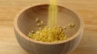 Mung Dal sarı fasulye ahşap masada ahşap kaseye dökülüyor.