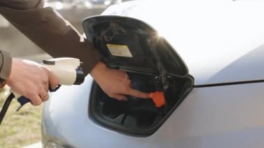Kafkasyalı bir erkeğin elektrikli bir arabayı açarken, soket kapağını şarj ederken ve şarj aletini takarken yakın çekim görüntüsü. Adam modern sıfır emisyon otomobilini şarj ediyor