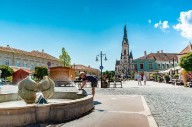 KOSZEG, HUNGARY - 14 Ağustos 2021: Güneşli, bulutlu bir yaz gününde Kutsal Kalp Kilisesi veya Koszegi Jezus szive plebaniatwork ve Main Squre veya Fo ter 'deki insanlar.