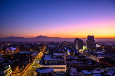 Gün batımında gökdelenden Ljubljana şehrine bakın. Arka planda dağlar var..