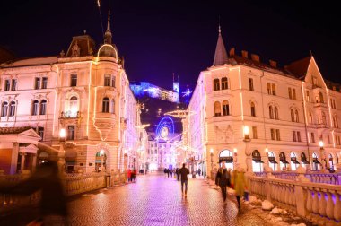 LJUBLJANA, SLOVENIA - 15 HAZİRAN 2022: Tromostovje Üçlü Köprüsü 'nde, arka planda Ljubljana Şatosu ile birlikte gece tatilinde yürüyen insanları izleyin