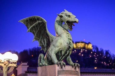 Ünlü Ejder Köprüsü ve Ejderha heykeli Zmajski 'yi gece Slovenya, Avrupa' daki Ljubljana şatosunun arka planında görüyorsunuz..