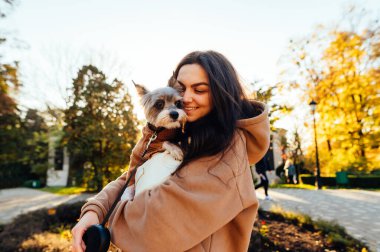 Neşeli ve güzel bir kadın güneşli bir günde Yorkshire teriyerine sarılıyor ve şehir parkında yürürken gülümsüyor..