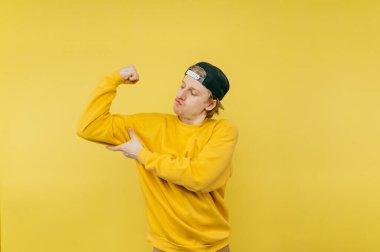 Parlak kazaklı genç adam sarı bir arka planda elinde bir banka kartıyla duruyor, kameraya bakıyor yüzünde bir gülümsemeyle ve şöyle bir jest yapıyor:.