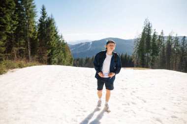 Gündelik giysiler içindeki bir adam, ılık bir bahar gününde karlı dağlarda güzel bir manzaranın arka planına karşı yürür. Aktif dinlenme dağlarda.