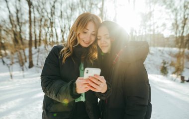 Sıcak, siyah kıyafetli itfaiyeciler güneşli bir günde bir kış parkında durup yüzlerinde gülümsemeyle akıllı telefon ekranına bakarlar..