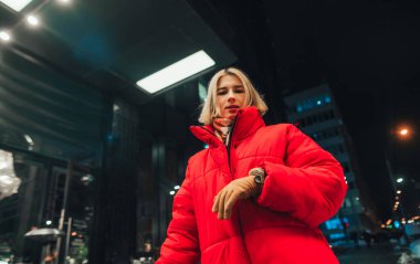 Kırmızı kışlık ceketli şık bir kadının portresi şehir manzarasının arka planında, kameraya poz veriyor.