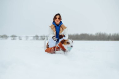 Karlı bir arazide Jack Russell 'ın köpeğiyle oynayan pozitif kadın sahibi gülümsüyor ve kameraya bakıyor..