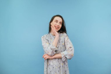 Güzel elbiseli ve diş teli takan, yüzünde gülümseme olan, mavi arka planda soyutlanmış, başka tarafa bakan ve gülümseyen hoş bir bayan..