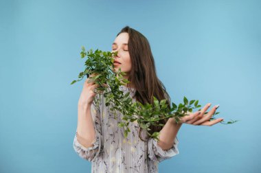 Güzel bir kadın ellerinde kıvırcık bir bitki tutar ve gözlerini kapatarak kokuyu içine çeker..