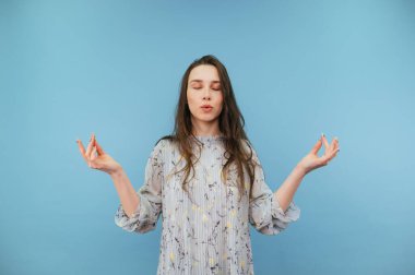 Sakin bayan meditasyon yapıyor mavi arka planda gözleri kapalı ve sakince nefes alıyor..