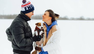 Kışın sokakta, kollarında küçük bir köpekle birbirlerine gülümseyen mutlu bir çift..