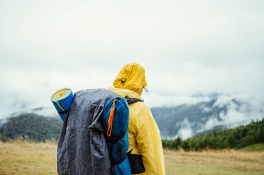 Sırtında sırt çantasıyla, Karpatlar 'ın sisli arka planında, dağlarda duran yağmurlu havada bir erkek turist..