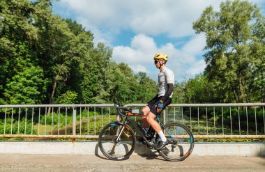 Erkek sporcu, nehrin arka tarafındaki köprüde bisikletle duruyor ve antrenmandan sonra dinleniyor..