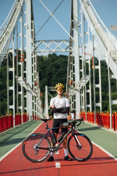Photo of a professional cyclist in a bicycle equipped with a bicycle on the background of a beautiful urban view, looking at the camera.