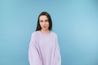 Mavi arka planda eşofmanlı güzel bir kadının portresi duruyor ve ciddi bir yüzle kameraya bakıyor..