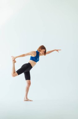 Mavi bluzlu ve şortlu atletik bayan ciddi bir yüzle beyaz arka planda esneme hareketleri yapıyor. Kadın antrenman yapıyor. izole.