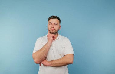 Mavi bir arka planda duran sakallı, ciddi bir yüzle kameraya bakıp şöyle düşünen düşünceli bir adam..