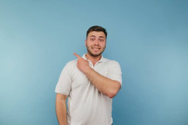 Sıradan giyinmiş duygusal sakallı bir adam mavi bir arka planda durur ve fotokopi alanında parmağını ve anlamlı yüzünü gösterir..