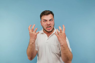 Tüylü kötü bir adamın portresi mavi bir arka planda, beyaz tişörtlü, kameraya bakıyor ve sinirleniyor..