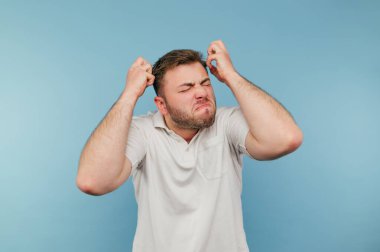 Umutsuzluk içinde kılları olan kızgın adam beyaz tişört giyen mavi arka planı izole etti. Kızgın adam duvarın arkasında gergin.