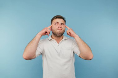 Sakallı komik bir adam şakağında parmaklarını gösteriyor ve ciddi bir yüz ifadesiyle başka yere bakıyor..