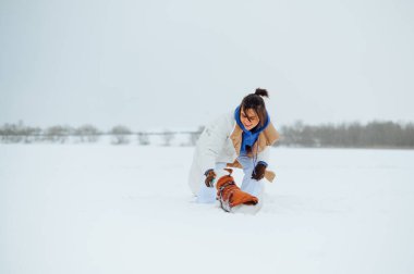 Karlı manzaralı bir arka planda yüzünde gülümseme olan, kışın yürüyüşe çıkmış, sıcak elbiseli olumlu bir kadın..