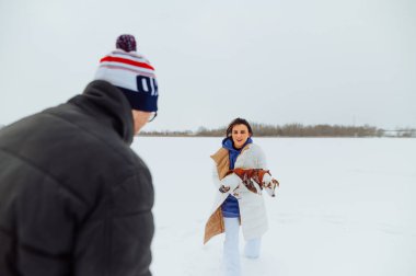 Mutlu kadın ve adam kış yürüyüşünde köpekle oynuyorlar donmuş karlı gölde, kollarında evcil hayvan tutan kadın..