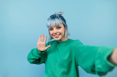 Mavi saçlı pozitif bir kız fotoğraf çeker ve kameraya gülümser. Mavi arka planda bir avuç dolusu tebrik eder..