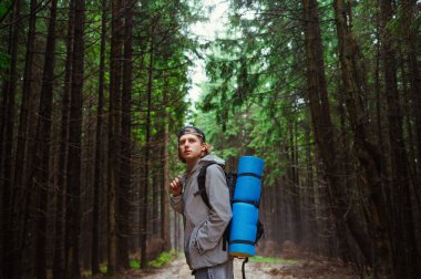 Yakışıklı bir adam ceketli ve sırt çantalı bir adam yürüyüş sırasında yolda duruyor ve sisli manzaranın arka planına bakıyor..