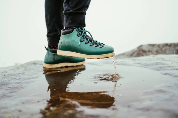 霧深い空に対して山の中で水たまりに立ってブーツで男性観光客の足の近い写真 — ストック写真