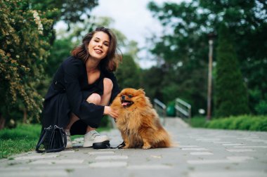 Parkta evcil hayvan taşıyan mutlu kadın köpek sahibi portresi, kameraya bakıyor ve gülümsüyor..