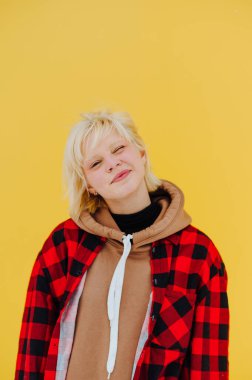 Sarı duvarın arka planında, tişörtlü ve sıradan elbiseli neşeli bir kızın portresi, kameraya bakıyor ve göz kırpıyor. Dikey