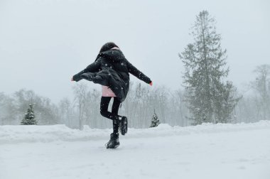 Sıcak, siyah ceketli kadın kar yağarken, kış mevsiminde dışarıda eğleniyor. Güzel, karlı bir manzaranın karşısında dönüyor..