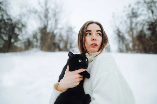 Atraktivní Žena Černou Kočkou Náručí Oblečená Bílém Pleteném Svetru Stojí — Stock fotografie