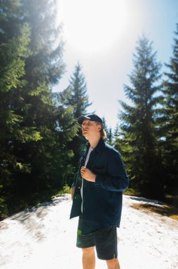 Genç erkek yürüyüşçü günlük giysiler ve şortlar içinde dağlarda karların üzerinde kozalaklı ağaçların üzerinde seyahat ederken..