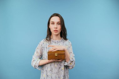 Elinde ahşap bir kutu olan hoş bir bayan mavi bir arka planda izole edilmiş, ciddi bir yüzle kameraya bakıyor..