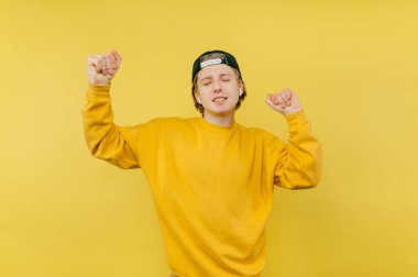 Pozitif adam kablosuz kulaklıkla müzik dinliyor ve sarı arka planda yüzünde bir gülümsemeyle dans ediyor. İzole edilmiş