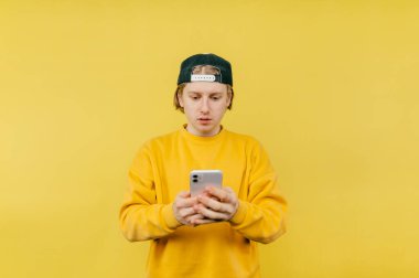 Şapkalı yakışıklı, sarı arka planda ciddi bir yüzü olan akıllı telefon kullanıyor. İzole edilmiş