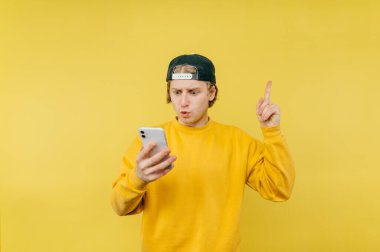 Şapkalı ve renkli tişörtlü bir adam akıllı telefon kullanıyor ve sarı arka planda şok olmuş bir yüzle fotokopi alanını işaret ediyor..