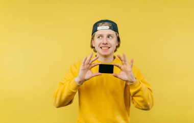 Elinde banka kartıyla sarı arka planda izole edilmiş, yüzünde bir gülümsemeyle yüzünü çeviren olumlu genç bir adam..
