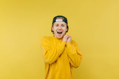 Sarı arka planda mutlu duran şapkalı ve sarı kazaklı neşeli adamın portresi ve açık ağızlı ve mutlu bir yüzle kameraya bakması..