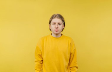 Sarı kazaklı yakışıklı genç adam sarı arka planda izole edilmiş, ciddi bir yüzle kameraya bakıyor..