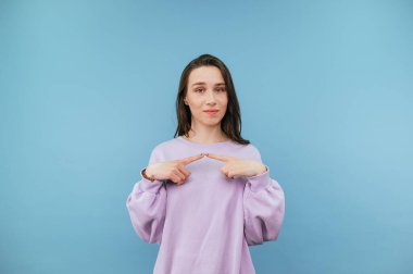 Mor kazaklı tatlı bayan mavi arka planda kızgın, alçakgönüllülükle kameraya bakıyor alaycı bir gülümsemeyle..